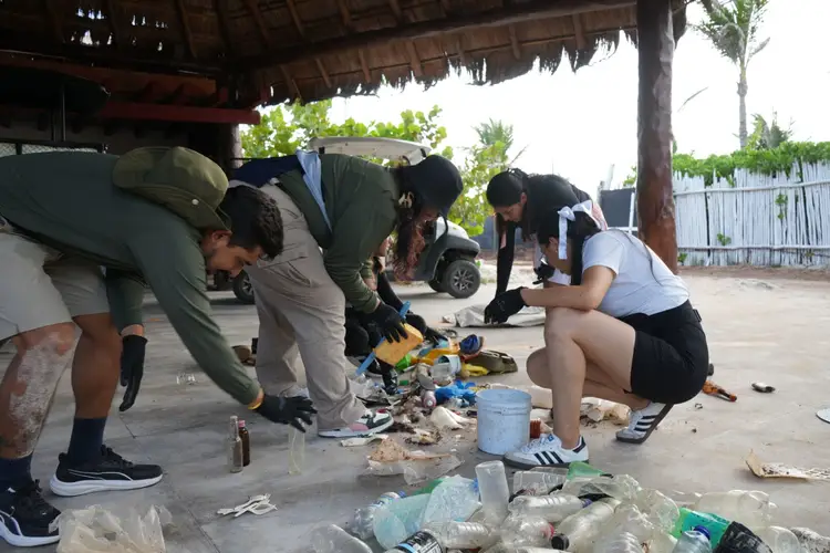Group of people sorting and collecting plastic waste and debris under a covered structure in an outdoor area