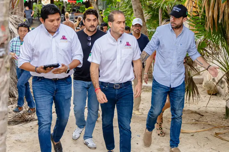 A group of men walks along a sandy path lined with palm trees while others observe in the background A group of men walks along a sandy path lined with palm trees while others observe in the background