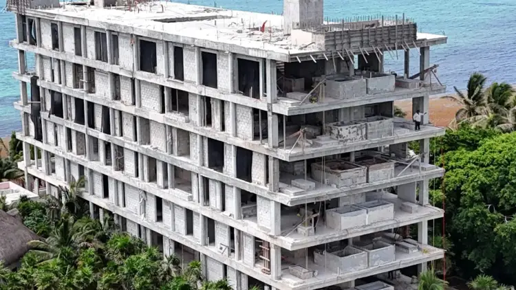 Concrete multi-story residential building under construction on a beachfront lot, with ocean visible in the background