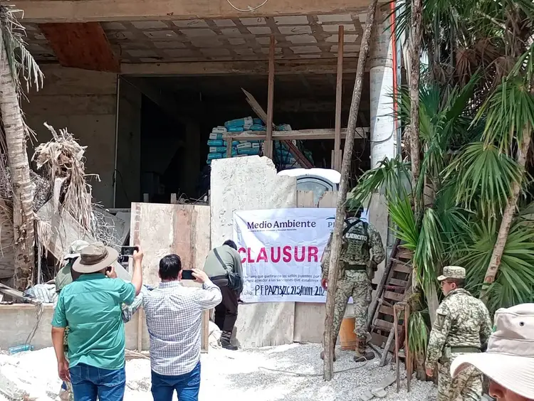 Officials and workers stand outside a shuttered construction site with a closure notice posted on materials and equipment stacked near the entrance