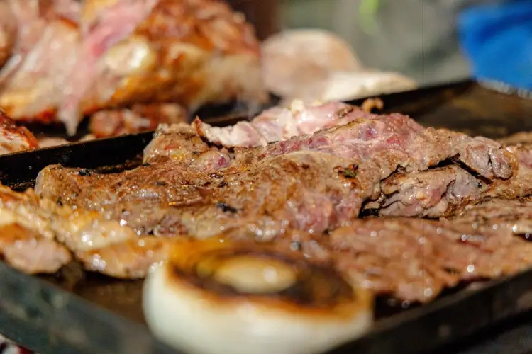 Grilled meat steaks cook on a hot surface with onion slices nearby