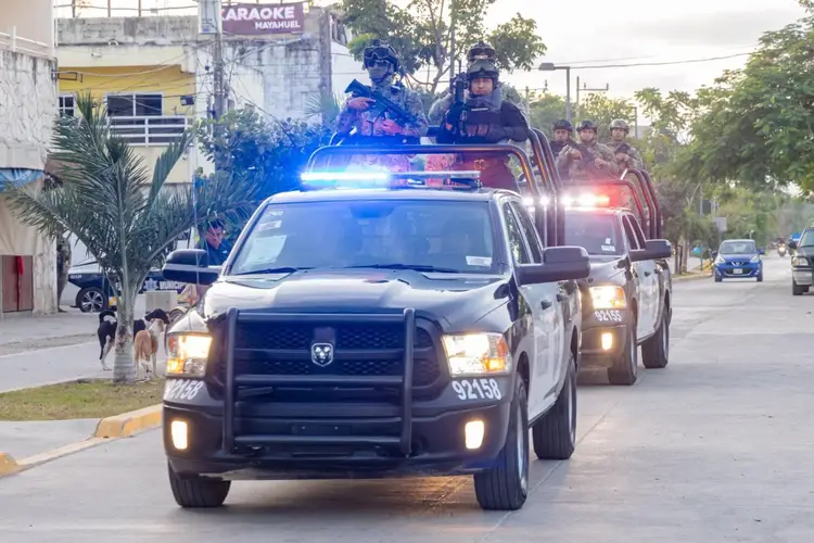 Police vehicles with lights activated drive down a residential street while officers stand in the truck bed