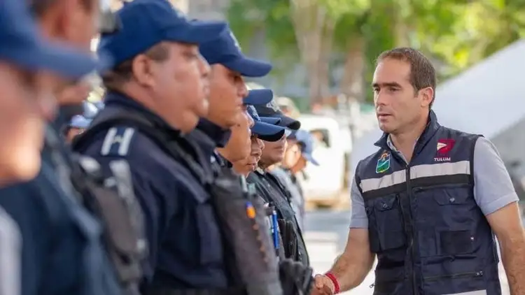 A man in a dark vest with patches speaks with uniformed officers wearing blue caps and jackets outdoors