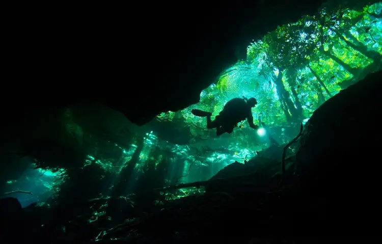 Scuba diver navigating through an underwater cave illuminated by green and blue light from above Scuba diver navigating through an underwater cave illuminated by green and blue light from above
