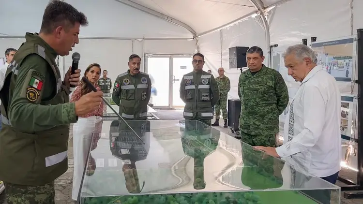 Military officers and civilians gather inside a tent around a table with a map display while one uniformed man speaks into a microphone Military officers and civilians gather inside a tent around a table with a map display while one uniformed man speaks into a microphone