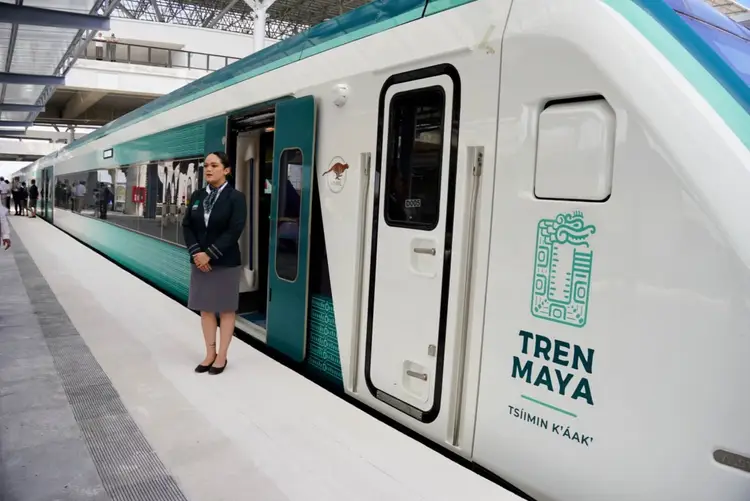 A woman in business attire stands at the open door of a teal and white train stopped at a platform inside a station A woman in business attire stands at the open door of a teal and white train stopped at a platform inside a station
