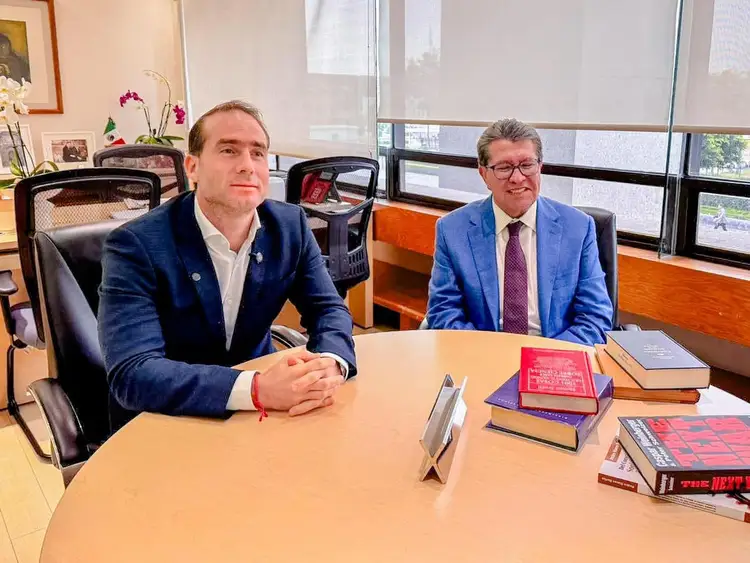 Two men in business attire sit at a conference table in an office with large windows overlooking a city skyline Two men in business attire sit at a conference table in an office with large windows overlooking a city skyline