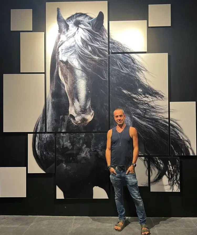 Man standing in front of a large mural depicting a dark horse with flowing mane surrounded by blank canvas panels on a black wall Man standing in front of a large mural depicting a dark horse with flowing mane surrounded by blank canvas panels on a black wall
