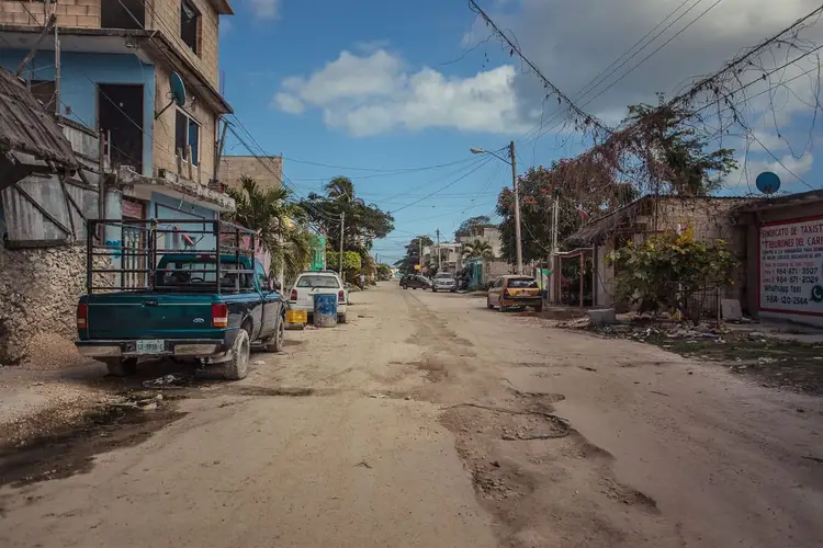 A pickup truck and other vehicles parked along an unpaved street lined with modest buildings and palm trees A pickup truck and other vehicles parked along an unpaved street lined with modest buildings and palm trees