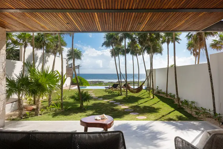 Beachfront property with palm trees, manicured lawn, and ocean view framed by covered patio area with dining furniture Beachfront property with palm trees, manicured lawn, and ocean view framed by covered patio area with dining furniture