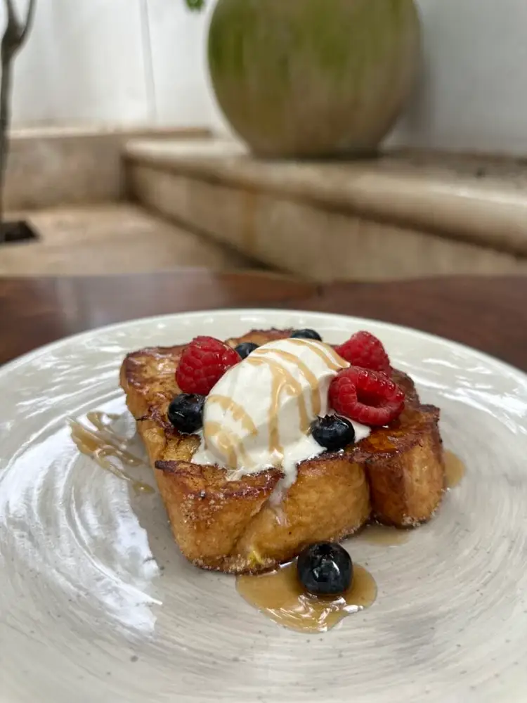 French toast topped with whipped cream, raspberries, blueberries and caramel drizzle on a white plate French toast topped with whipped cream, raspberries, blueberries and caramel drizzle on a white plate