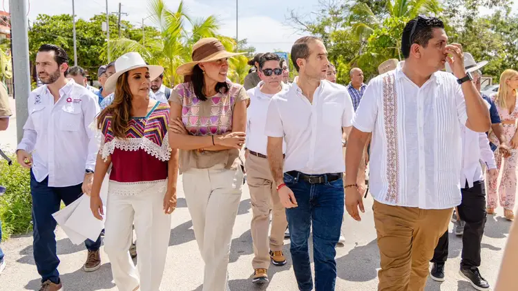 A group of people walk together outdoors during a daytime event, with tropical vegetation and palm trees visible in the background A group of people walk together outdoors during a daytime event, with tropical vegetation and palm trees visible in the background