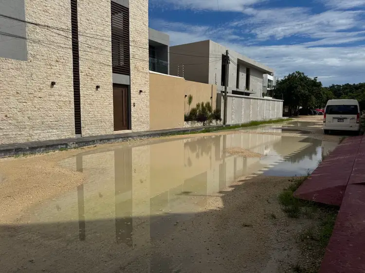 Murky water pools in front of modern residential buildings along a street lined with parked vehicles Murky water pools in front of modern residential buildings along a street lined with parked vehicles