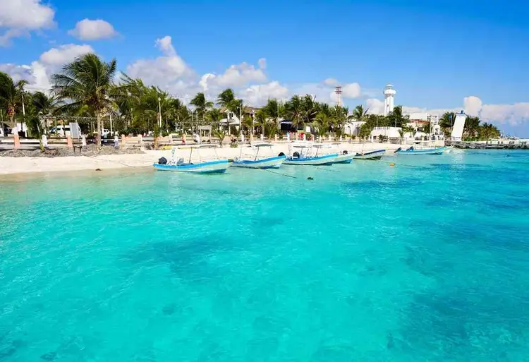 Fishing boats anchored in clear turquoise water near a sandy beach lined with palm trees and waterfront buildings Fishing boats anchored in clear turquoise water near a sandy beach lined with palm trees and waterfront buildings