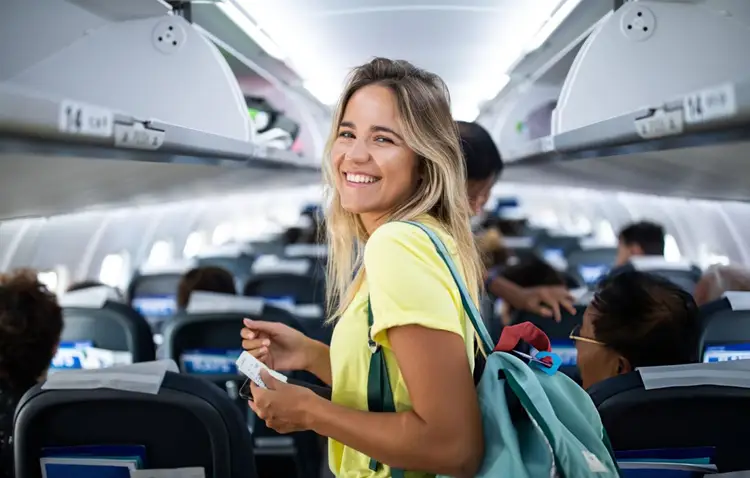 Woman in yellow shirt walking through airplane cabin with passengers seated in rows behind her