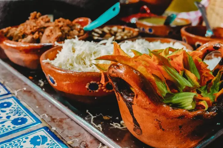 Grilled poblano peppers stuffed with cheese and topped with green onions sit on a dark plate next to shredded white cheese and other Mexican dishes