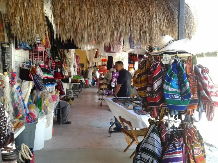 Vendor stall with thatched roof displaying colorful textiles and handcrafted goods along a covered market walkway Vendor stall with thatched roof displaying colorful textiles and handcrafted goods along a covered market walkway