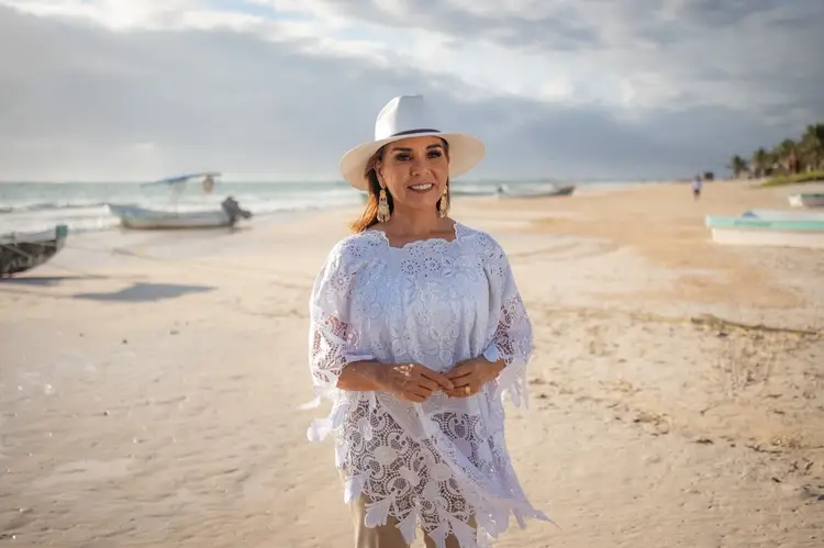 Woman in white lace clothing and hat standing on a sandy beach with fishing boats in the background Woman in white lace clothing and hat standing on a sandy beach with fishing boats in the background
