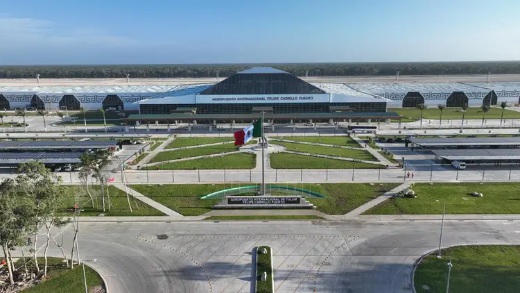 Aerial view of an airport terminal with a distinctive domed roof, surrounded by manicured grounds, roadways, and forested areas in the distance