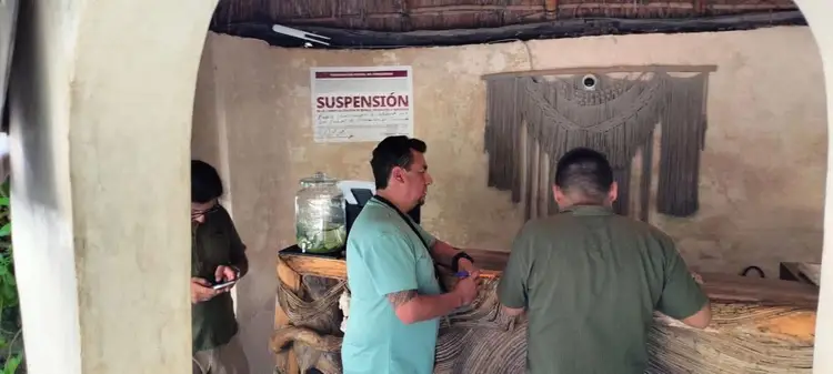 Two officials inspect a modest room with a "Suspensión" notice posted on the wall