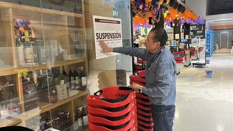 Man in gray shirt points at a display case containing bottles in what appears to be a retail store interior