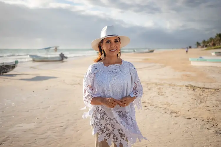 Woman in white lace dress and cowboy hat stands on a beach with fishing boats and ocean in the background Woman in white lace dress and cowboy hat stands on a beach with fishing boats and ocean in the background