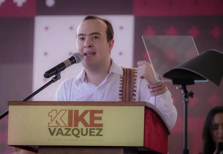 Man in white shirt with embroidered details speaking at a podium with microphone during a political event