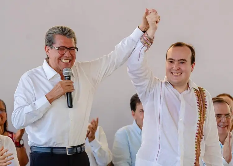 Two men in white shirts raise their joined hands in celebration while standing before an audience indoors