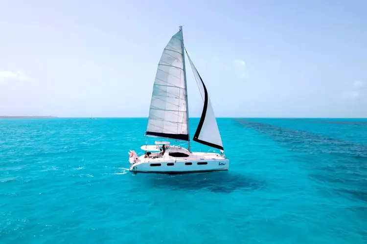 Sailboat with white and blue sails anchored in clear turquoise water under a blue sky