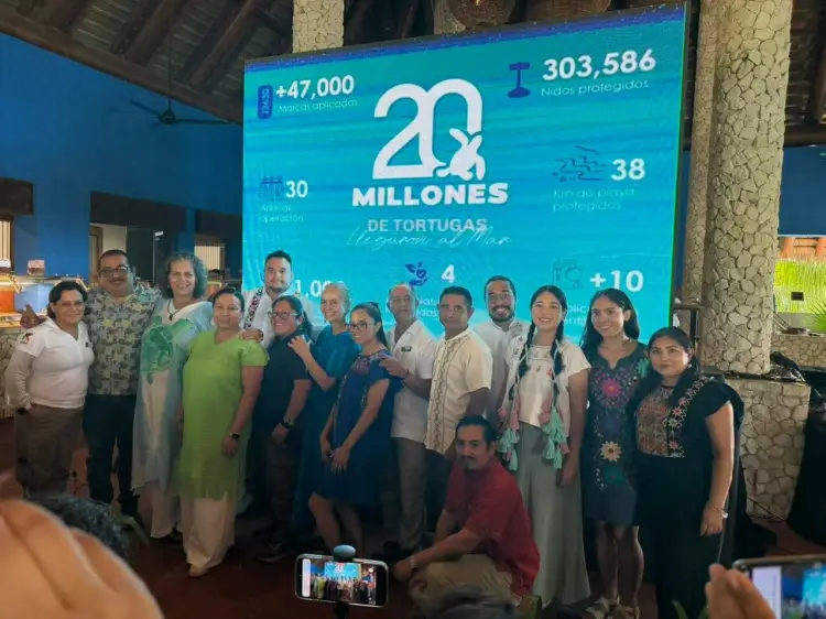 A group of people pose together in front of a large teal display showing statistics about sea turtle hatchlings released, with the number 20 million prominently
