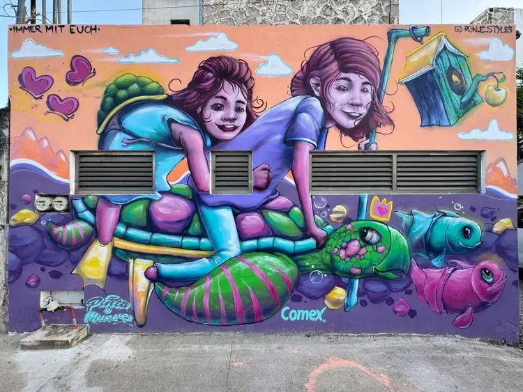 Mural on a building wall depicting two illustrated figures with purple hair surrounded by colorful sea creatures and whimsical objects against an orange and pur