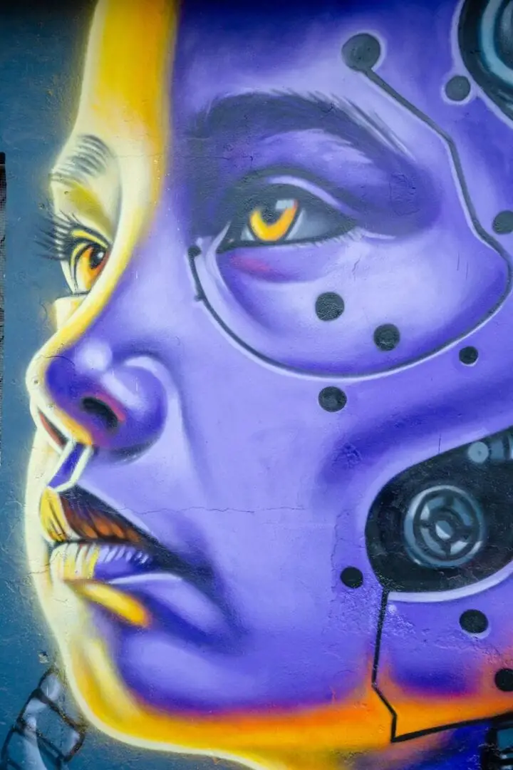 Mural depicting a purple face with yellow accents, glowing eyes, and mechanical elements on an urban wall