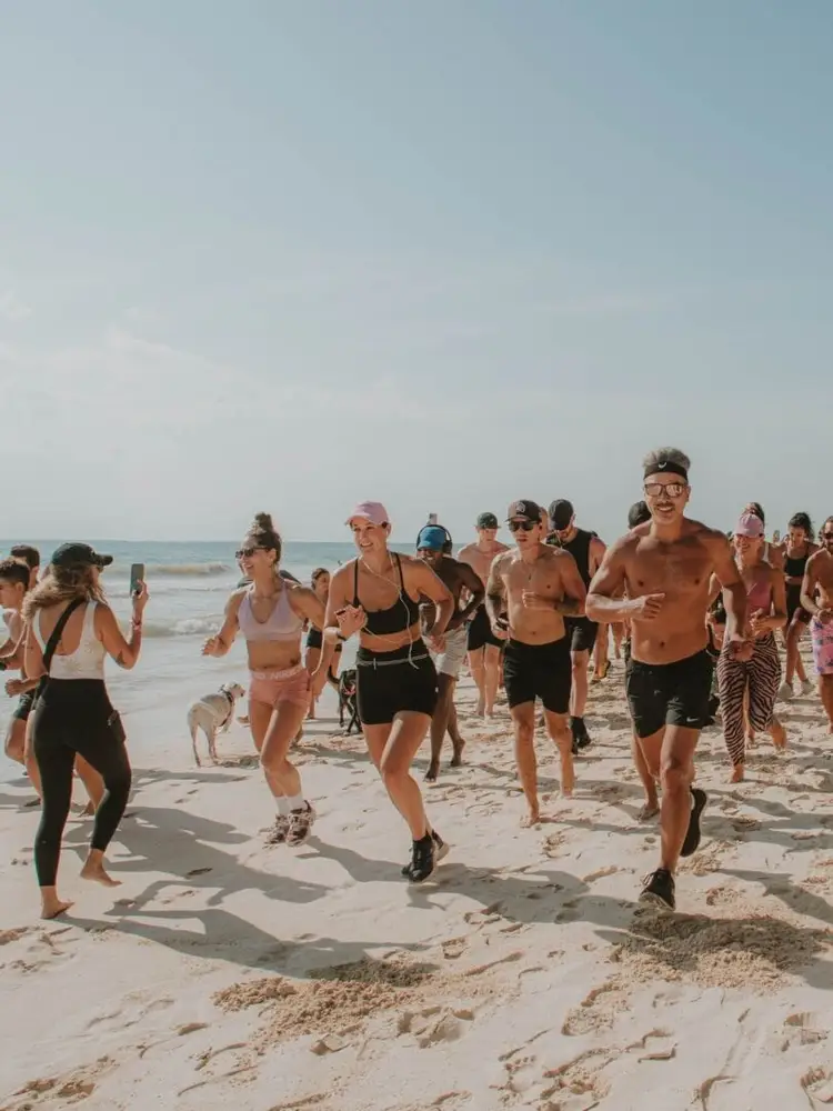 A group of runners jogs along a sandy beach with the ocean visible in the background under a clear sky A group of runners jogs along a sandy beach with the ocean visible in the background under a clear sky