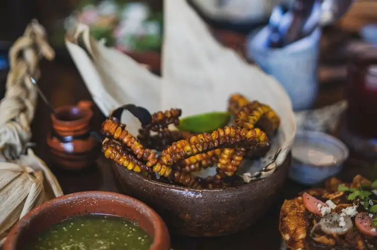 Roasted grasshoppers sit in a dark ceramic bowl next to a green sauce and other traditional Mexican dishes Roasted grasshoppers sit in a dark ceramic bowl next to a green sauce and other traditional Mexican dishes