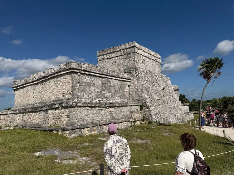 Visitors walk toward a stone fortress structure with a central tower under clear blue sky, with a palm tree visible on the right and a rope barrier in the foreg Visitors walk toward a stone fortress structure with a central tower under clear blue sky, with a palm tree visible on the right and a rope barrier in the foreg