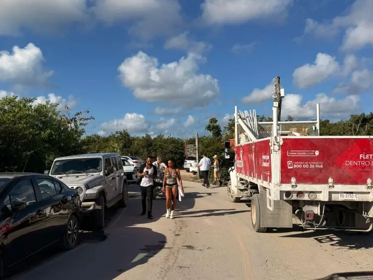 People stand on a roadside near parked vehicles and a red delivery truck under a blue sky with white clouds People stand on a roadside near parked vehicles and a red delivery truck under a blue sky with white clouds