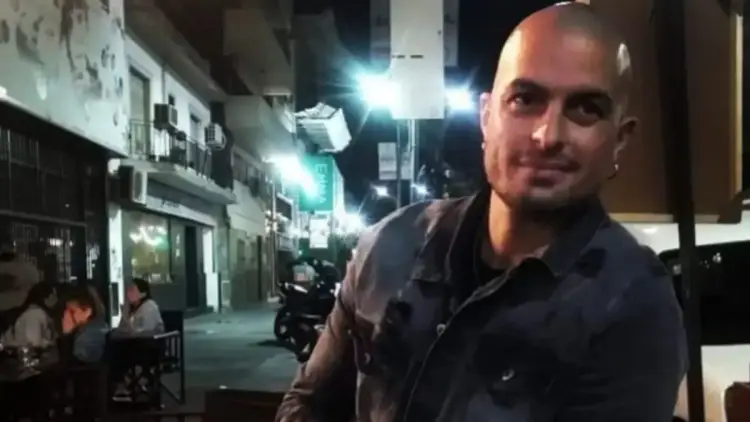 Man in dark shirt stands on a nighttime street lined with storefronts and bright lights