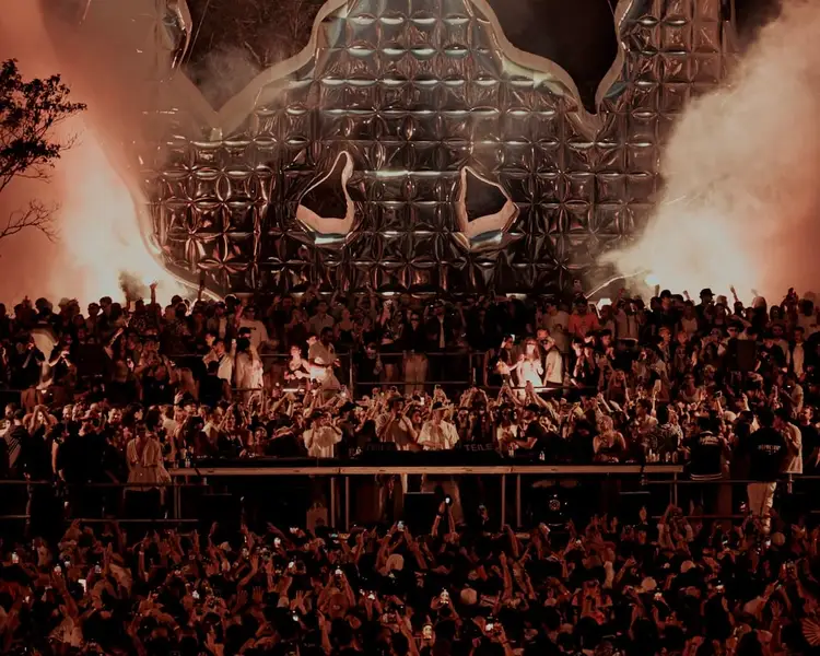 Large crowd of festival attendees gather before an elaborate skull-shaped stage structure with dramatic lighting and fog effects