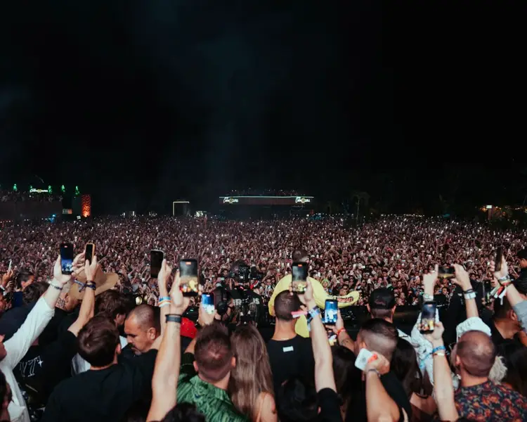 Large crowd of concertgoers holds up phones and cameras during a nighttime electronic music festival performance