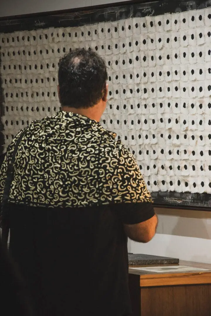 Person viewed from behind standing at a pegboard wall in an indoor gallery or exhibition space