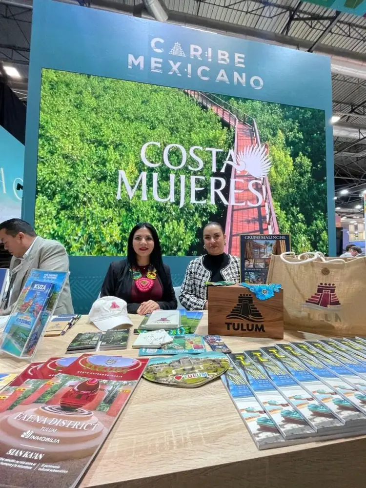 Staff members staff a tourism booth displaying promotional materials and souvenirs at an indoor trade show