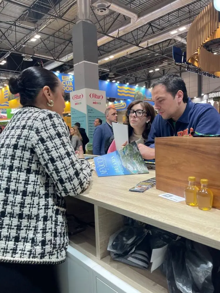 Man and woman at an exhibition booth talk with a visitor while displaying promotional materials and product samples