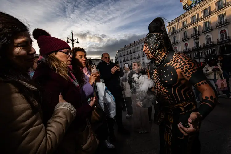 A person in elaborate jaguar-patterned body paint and costume interacts with onlookers in a city plaza lined with historic buildings