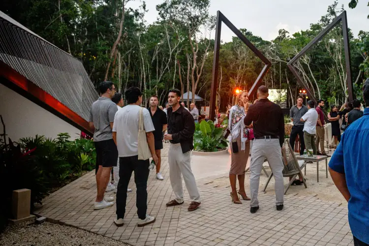 Guests mingle at an outdoor event in a jungle setting with modern architectural structures and tall trees surrounding a paved courtyard