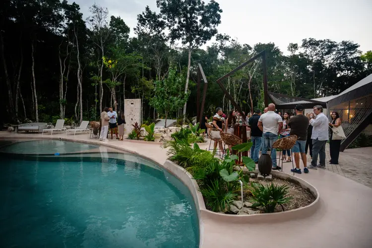 Guests gather around a swimming pool at an outdoor venue surrounded by tall trees and tropical vegetation