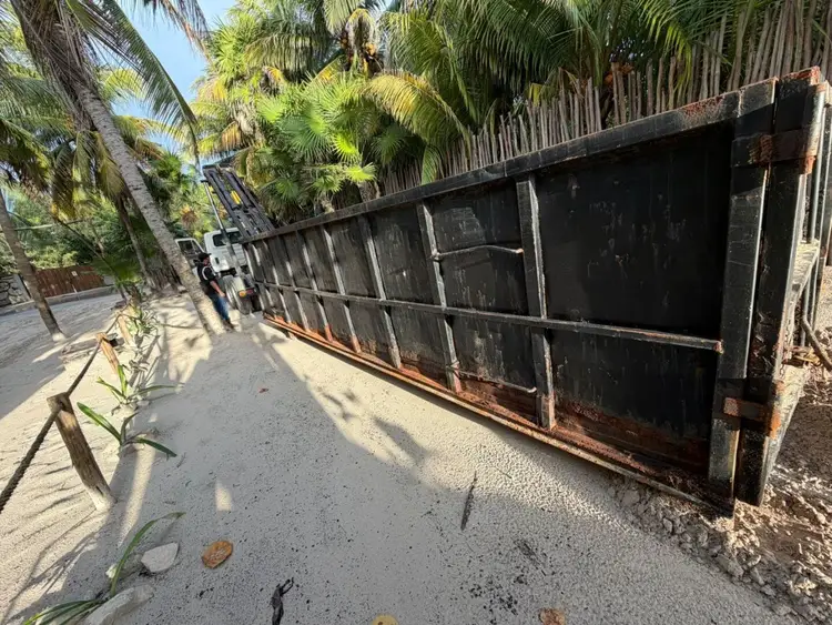 A weathered metal storage structure sits along a sandy path lined with palm trees and vegetation