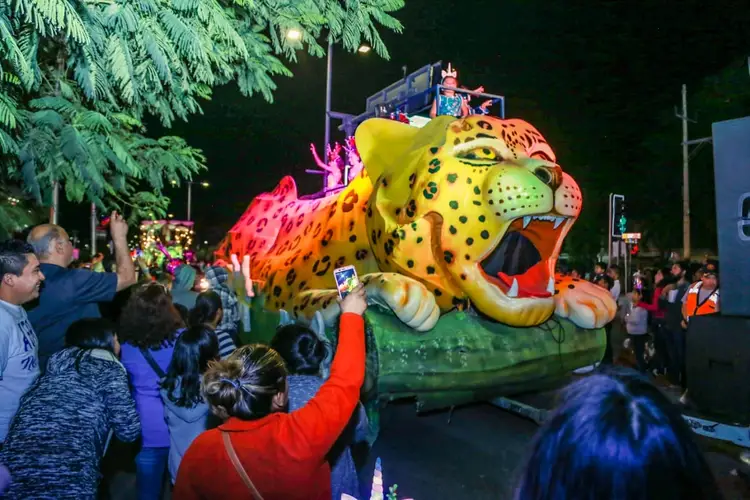Spectators watch a large illuminated leopard-shaped parade float at night during a carnival celebration