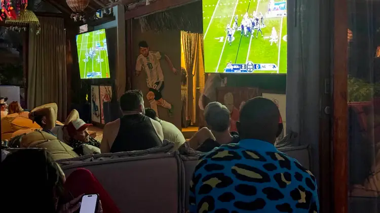 People watch a football game on large screens at an indoor venue with dark lighting and decorative elements D880CE9D-393E-4B2E-9740-8FCC64855108_1_201_a