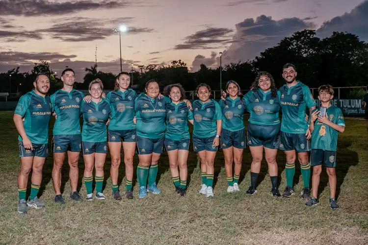 Rugby team in teal uniforms stands together on a field at dusk under floodlights Rugby team in teal uniforms stands together on a field at dusk under floodlights
