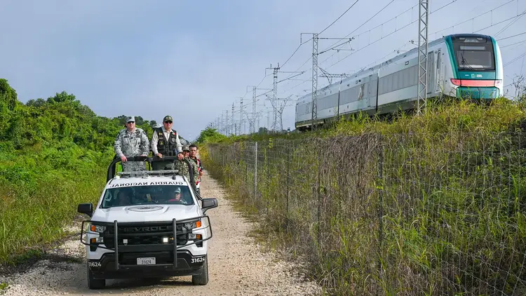 Border patrol officers on an all-terrain vehicle travel along a dirt road beside railroad tracks and vegetation image_1